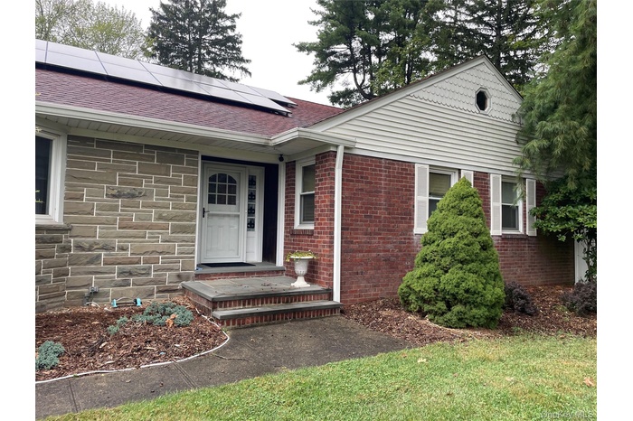 Entrance to property with roof mounted solar panels, roof with shingles, and brick siding