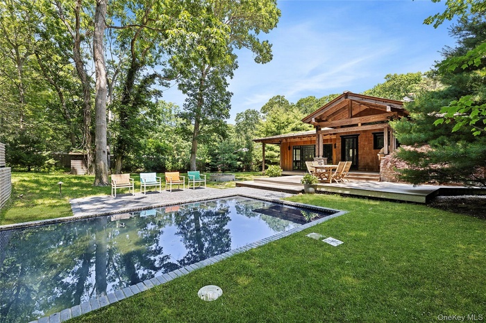 Outdoor pool with a deck, a yard, and view of wooded area