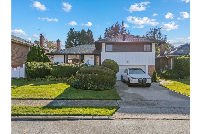 Tri-level home featuring driveway, a front lawn, brick siding, and a chimney