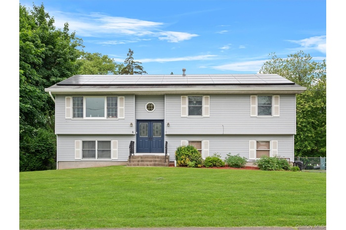 Split foyer home with roof mounted solar panels, a front yard, and entry steps
