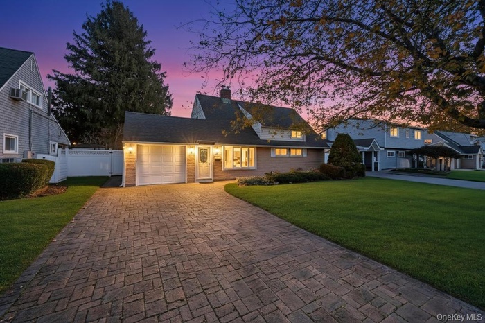 Cape cod-style house featuring a chimney, decorative driveway, and a garage