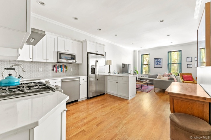 Kitchen featuring crown molding, appliances with stainless steel finishes, white cabinetry, open floor plan, and decorative backsplash