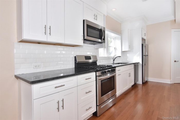 Kitchen featuring stainless steel appliances, white cabinetry, dark wood finished floors, decorative backsplash, and crown molding