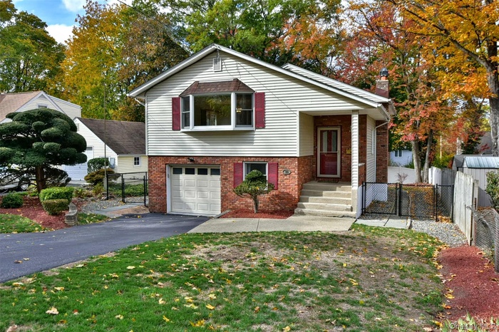 Tri-level home featuring a gate, brick siding, an attached garage, a chimney, and asphalt driveway