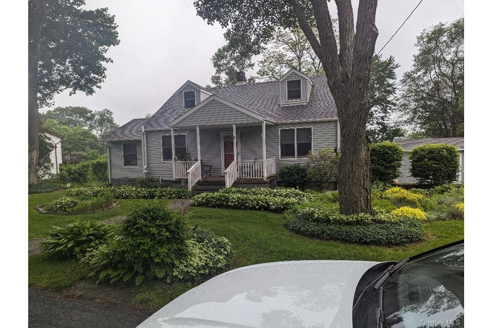 Cape cod house with a front yard, a chimney, and covered porch