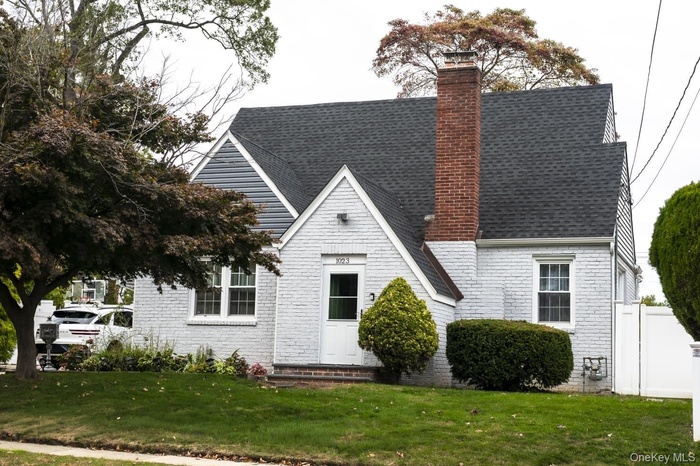 View of front of home with a chimney, brick siding, and roof with shingles