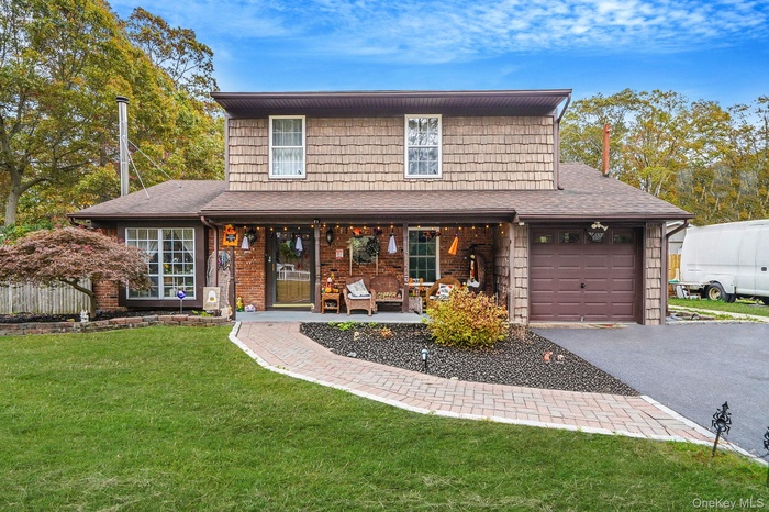 Traditional home featuring a front yard, covered porch, asphalt driveway, brick siding, and a shingled roof