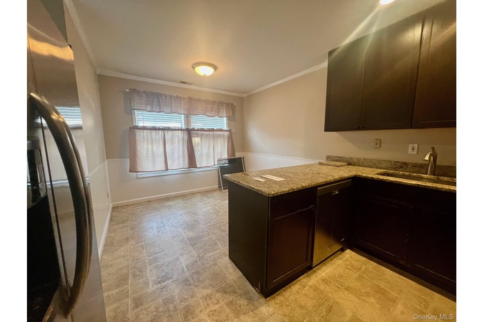 Kitchen featuring stainless steel appliances, ornamental molding, dark brown cabinets, light stone countertops, and a peninsula