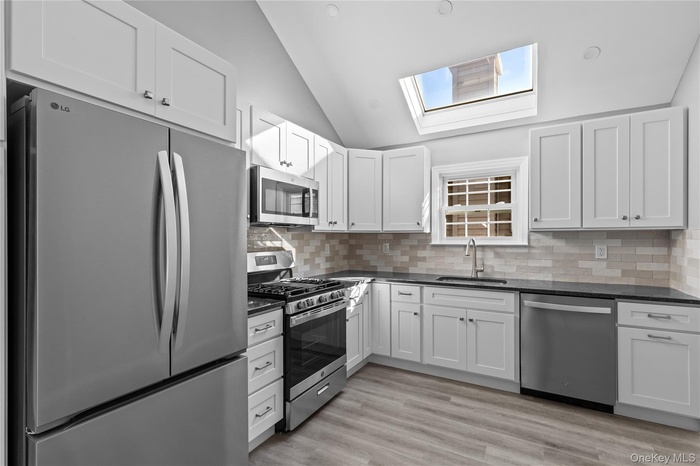 Kitchen featuring stainless steel appliances, lofted ceiling, white cabinetry, decorative backsplash, and light wood-style floors