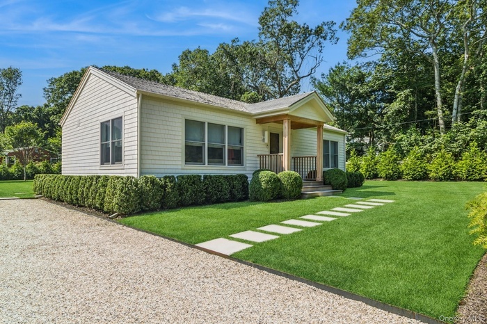 View of front of house with a front lawn, a porch, and view of wooded area