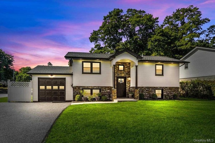 Split foyer home with driveway, stone siding, and a garage