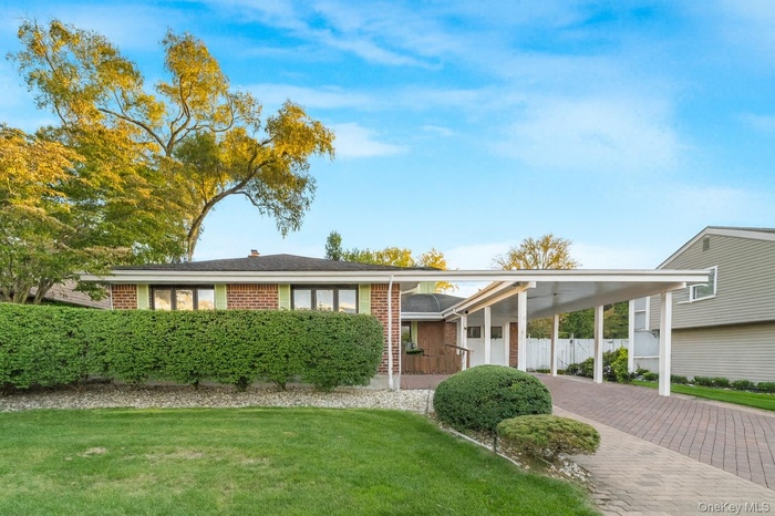 View of front facade featuring an attached carport, brick siding, a front lawn, and decorative driveway