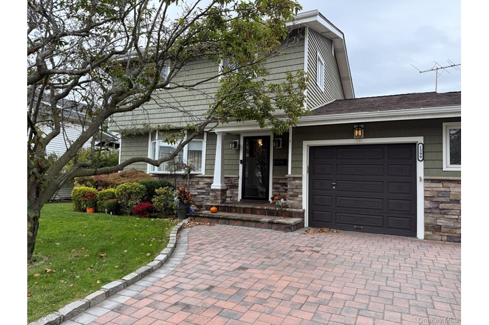 View of front of home featuring stone siding, a front yard, an attached garage, roof with shingles, and covered porch