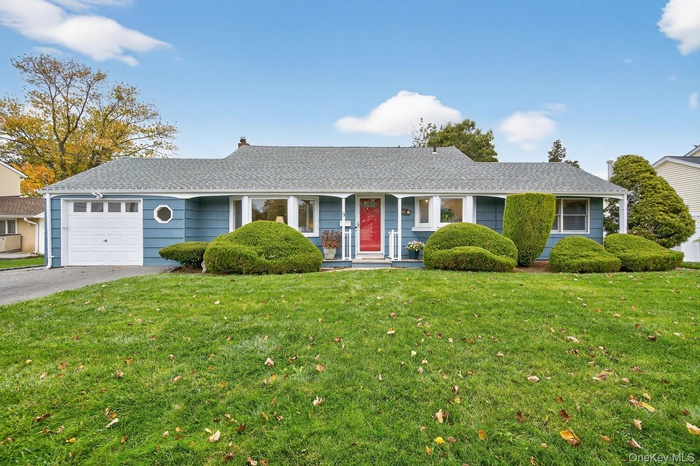 Ranch-style house with roof with shingles, a porch, a front yard, an attached garage, and driveway
