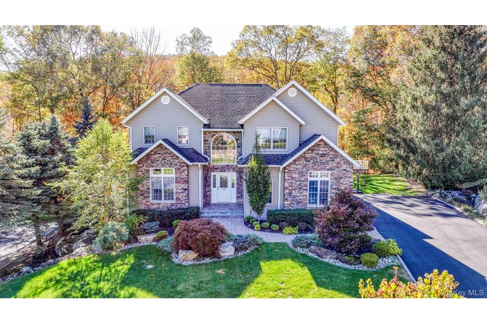 Traditional home with stone siding, a front lawn, a shingled roof, and driveway