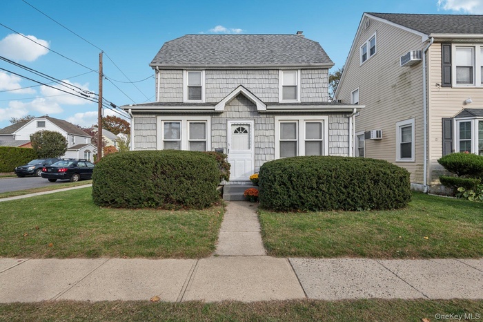 View of front facade featuring a front yard, roof with shingles, and a wall mounted AC