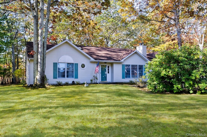 Single story home featuring a front lawn, a chimney, and view of scattered trees