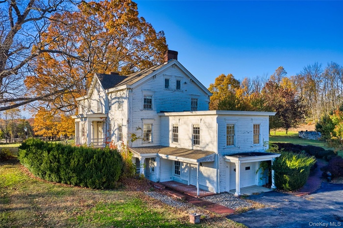 View of front facade featuring an attached garage, a chimney, a porch, and driveway