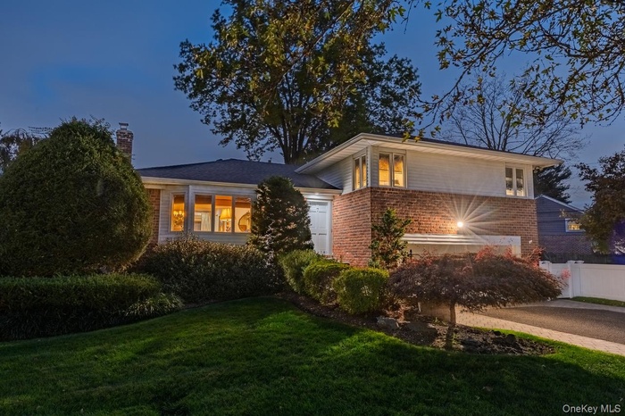 View of front facade featuring brick siding, a chimney, a garage, and driveway
