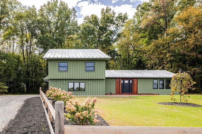 View of front of home with a metal roof, a front yard, view of scattered trees, and board and batten siding