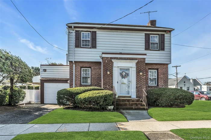View of front of house featuring a chimney, brick siding, driveway, and a garage