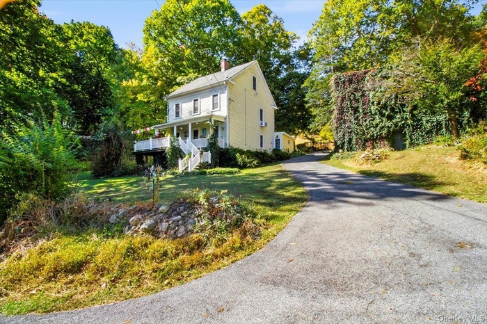View of front facade featuring a chimney, driveway, a front yard, view of scattered trees, and stairs