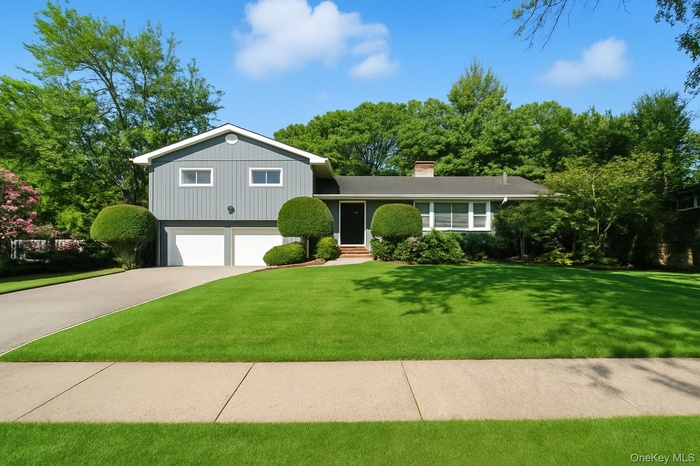Split level home featuring driveway, a chimney, a front lawn, and an attached garage