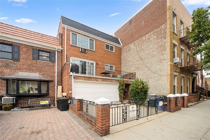 Rear view of house featuring driveway, a garage, brick siding, and a fenced front yard