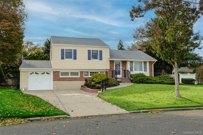 Split level home with driveway, an attached garage, brick siding, and a shingled roof