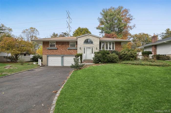 Split level home featuring asphalt driveway, a front yard, brick siding, and a garage