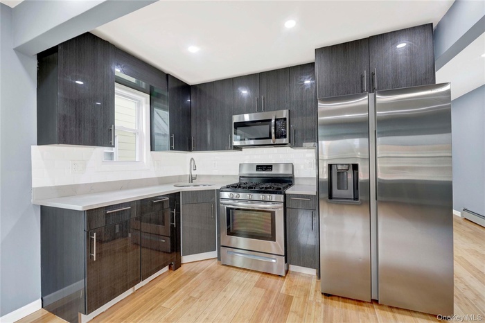 Kitchen featuring appliances with stainless steel finishes, modern cabinets, light wood-style floors, a baseboard heating unit, and decorative backspl