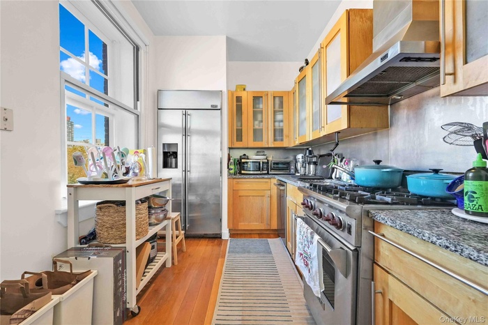 Kitchen with wall chimney exhaust hood, premium appliances, light wood-type flooring, and glass insert cabinets