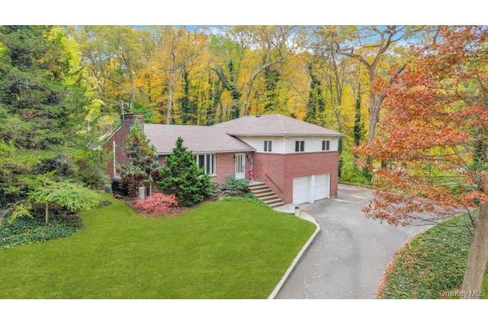 Split level home featuring brick siding, a front lawn, a chimney, driveway, and a garage