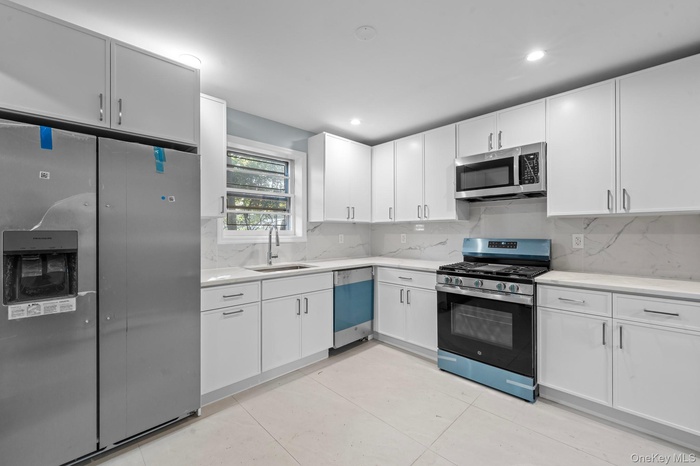 Kitchen featuring appliances with stainless steel finishes, tasteful backsplash, light tile patterned floors, white cabinetry, and light stone counter
