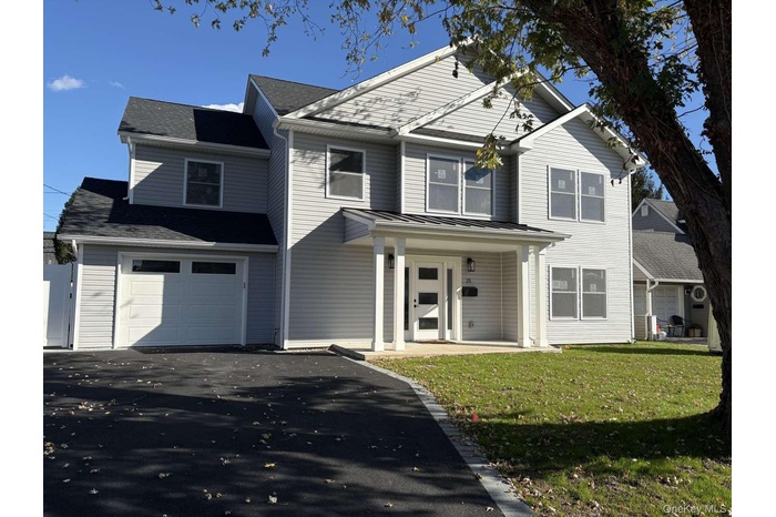 Traditional-style home with covered porch, asphalt driveway, a front lawn, a standing seam roof, and an attached garage