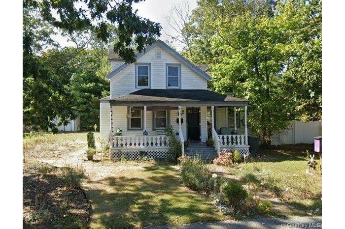 Farmhouse-style home featuring covered porch and a front lawn