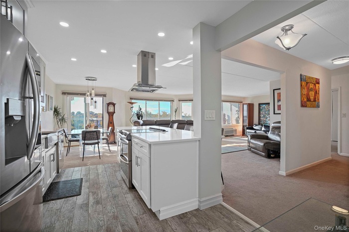 Your view from the front doorKitchen featuring stainless steel appliances, white cabinetry, island range hood, decorative light fixtures, and light st
