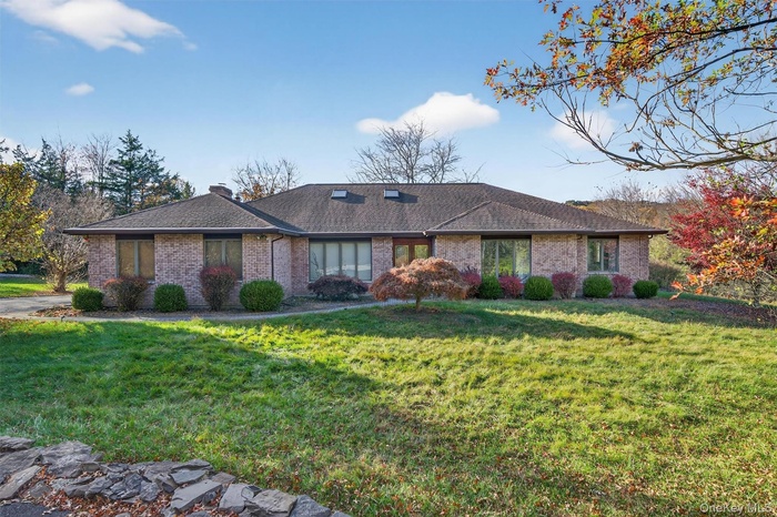 Single story home featuring a front yard, brick siding, a chimney, and roof with shingles