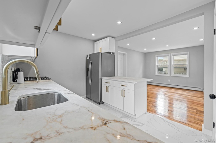 Kitchen with light marble finish flooring, stainless steel fridge with ice dispenser, light stone counters, a peninsula, and white cabinets