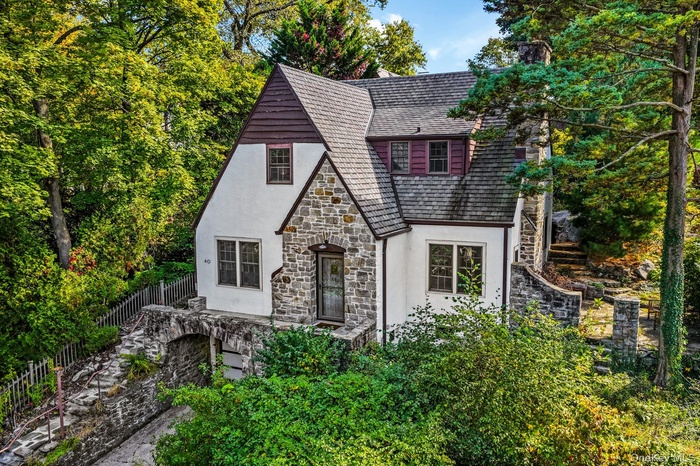 Tudor-style house featuring stone siding, stucco siding, stairway, a chimney, and a shingled roof