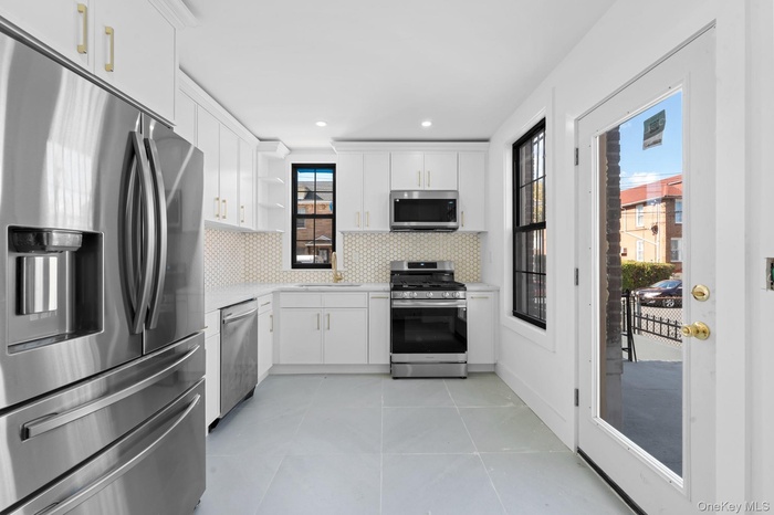 Kitchen featuring stainless steel appliances, open shelves, light tile patterned floors, backsplash, and white cabinetry