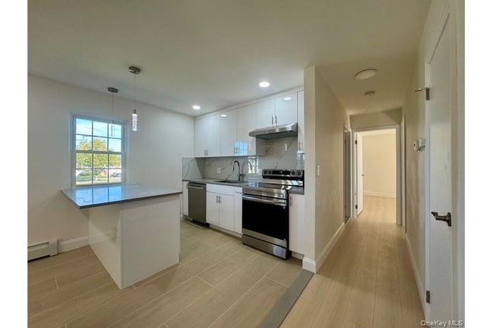 Kitchen featuring white cabinets, appliances with stainless steel finishes, light wood-type flooring, decorative backsplash, and recessed lighting