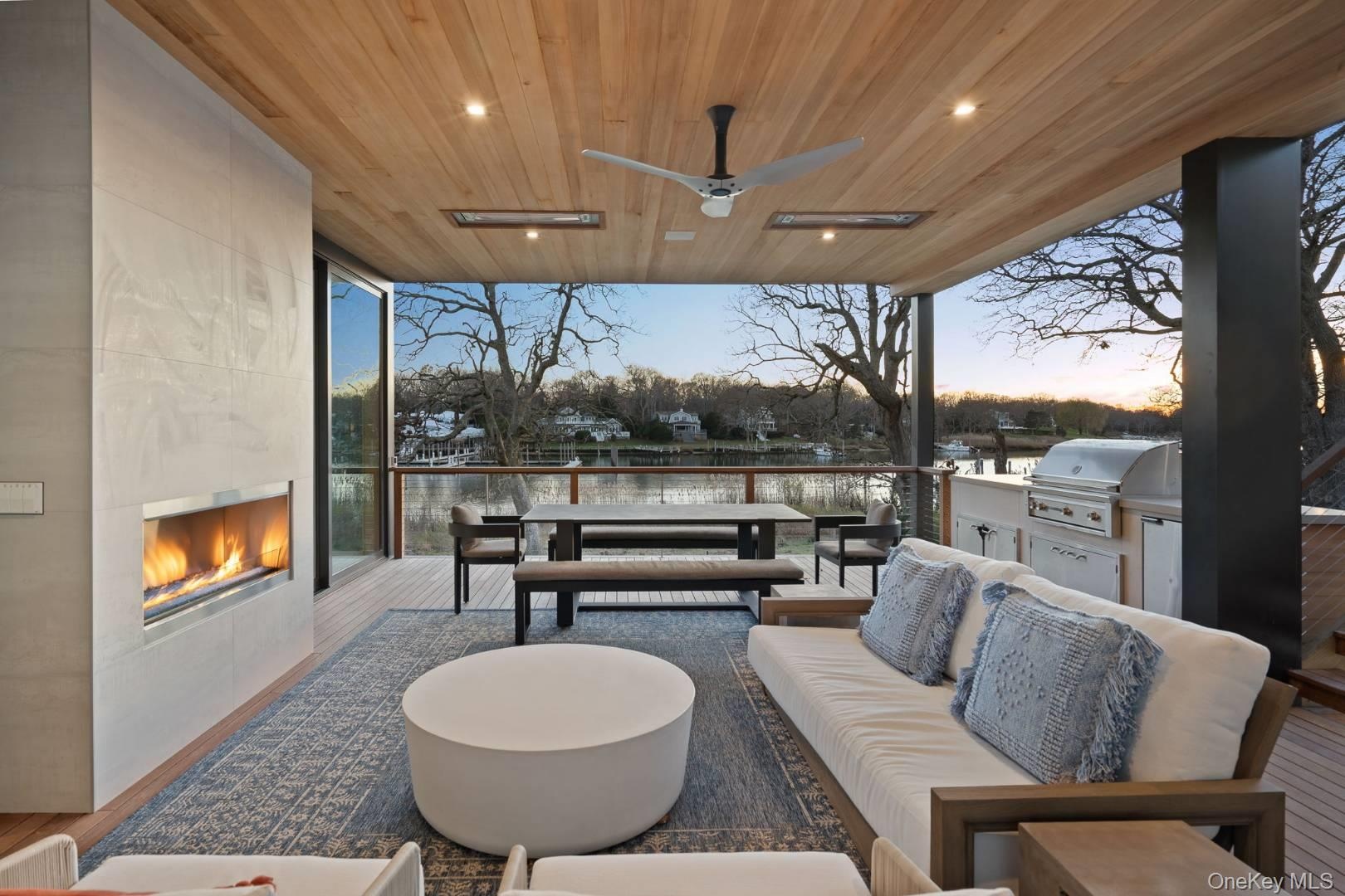 Patio terrace at dusk featuring an outdoor living space with a fireplace, ceiling fan, exterior kitchen, and a grill