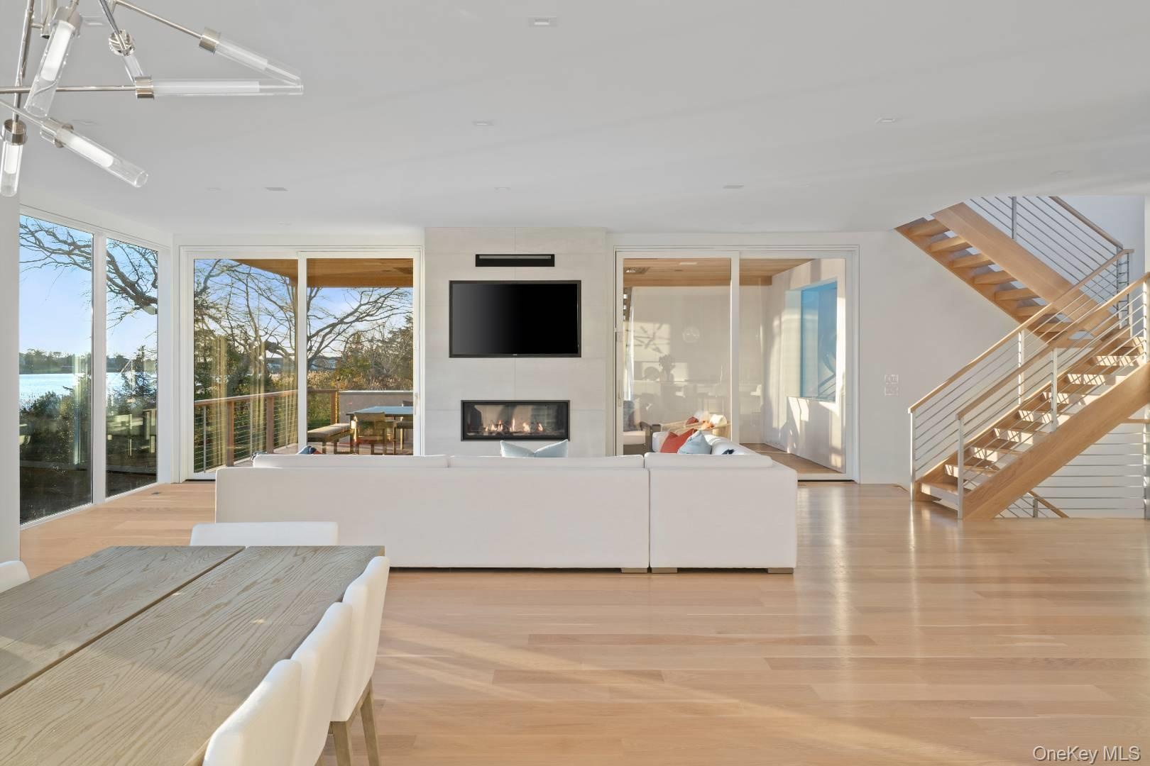 Living room with a large fireplace, light wood-type flooring, floor to ceiling windows, and an inviting chandelier