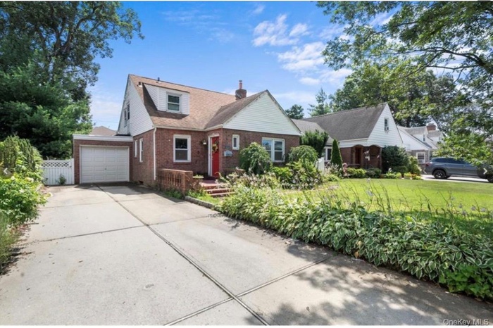 View of front of property featuring brick siding, driveway, a chimney, and a garage