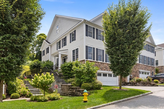 Colonial inspired home with stairway, stone siding, an attached garage, a front yard, and driveway