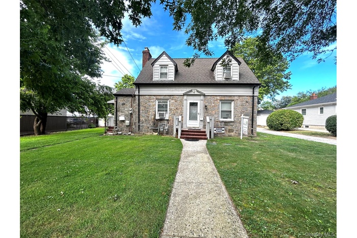 View of front of house with stone siding, a chimney, and a shingled roof
