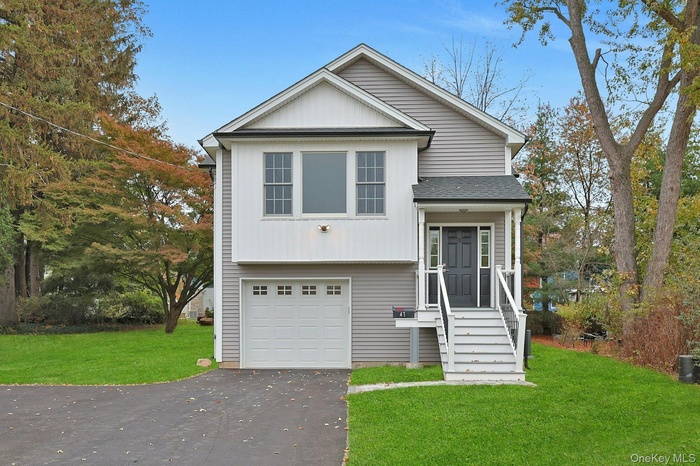 View of front of home with a front yard, asphalt driveway, a shingled roof, an attached garage, and board and batten siding