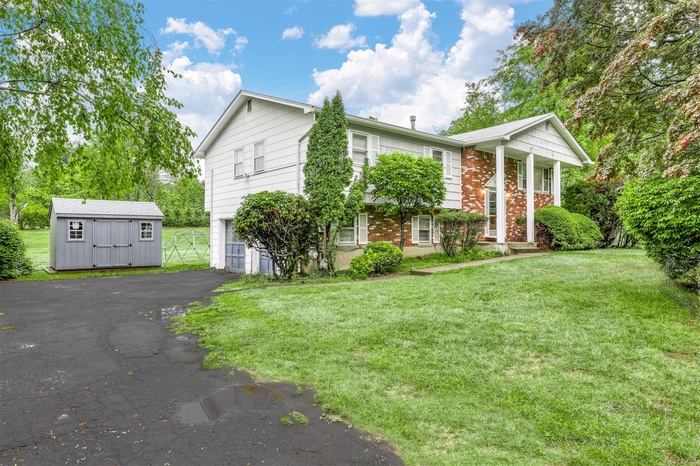 Bi-level home with an attached garage, an outbuilding, driveway, and a front lawn