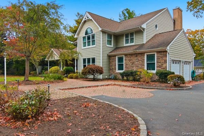 Traditional-style house with a chimney, stone siding, asphalt driveway, and roof with shingles